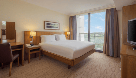 Image of a hotel room with a gap under the bed, bedside tables with light switches and phone, a dressing table with low mirror.