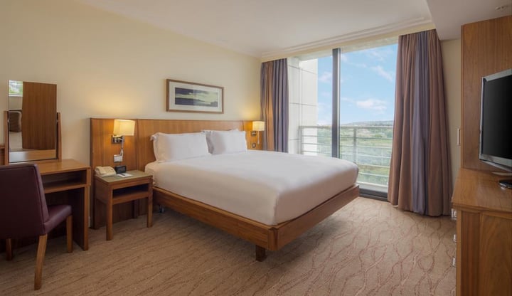 Image of a hotel room with a gap under the bed, bedside tables with light switches and phone, a dressing table with low mirror.