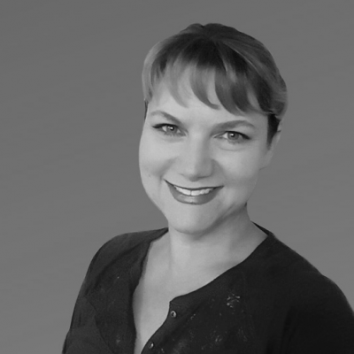 image shows a smiling woman with short dark hair wearing a black top. She has a warm, friendly expression on her face.